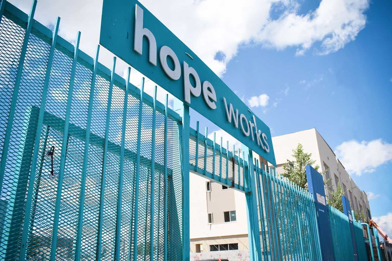 Teal gates at the front of the HopeWorks Day Shelter with a metal sign that reads “HopeWorks”.