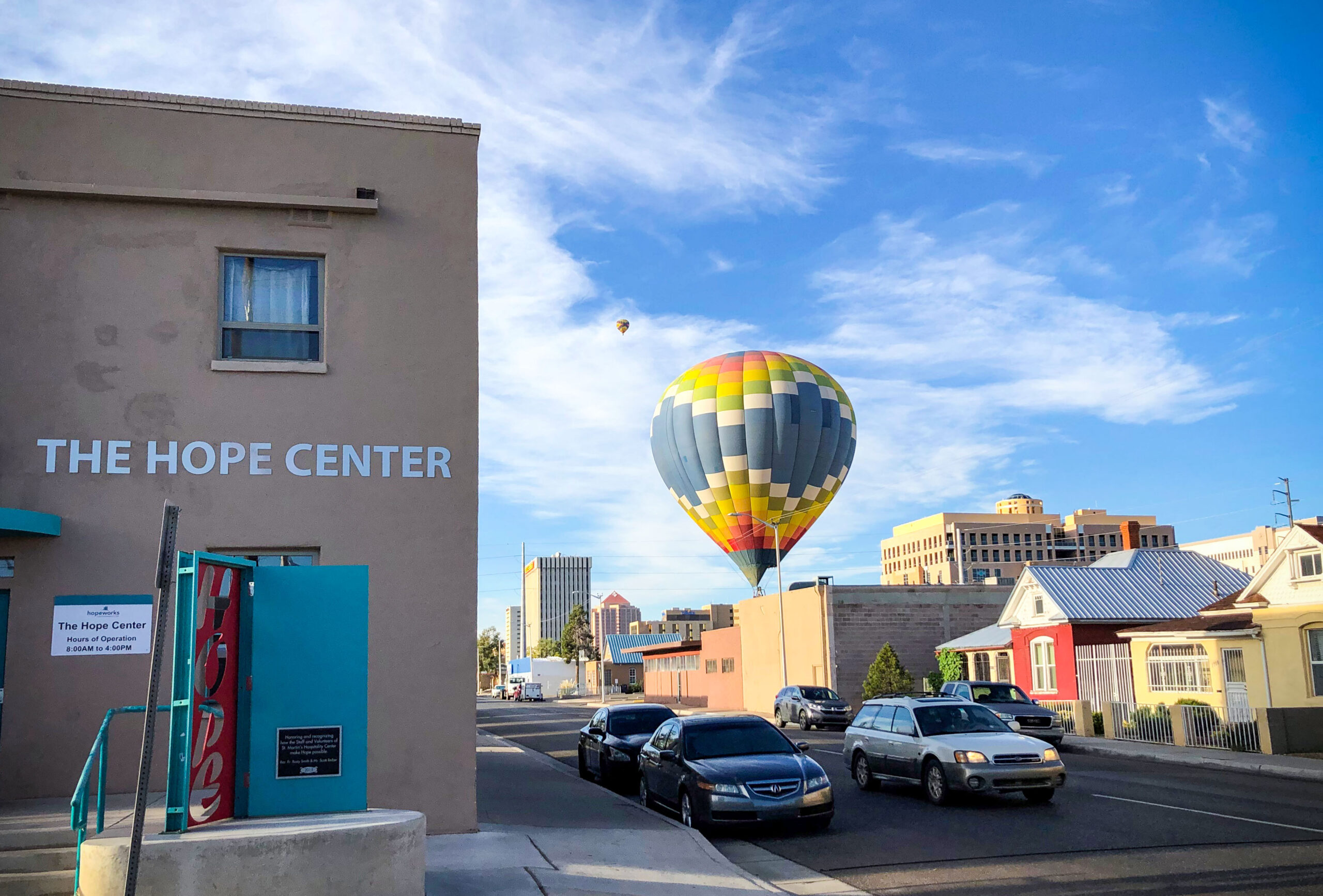 A multicolored hot air balloon floats above the adobe-colored Hope Center on a clear day.