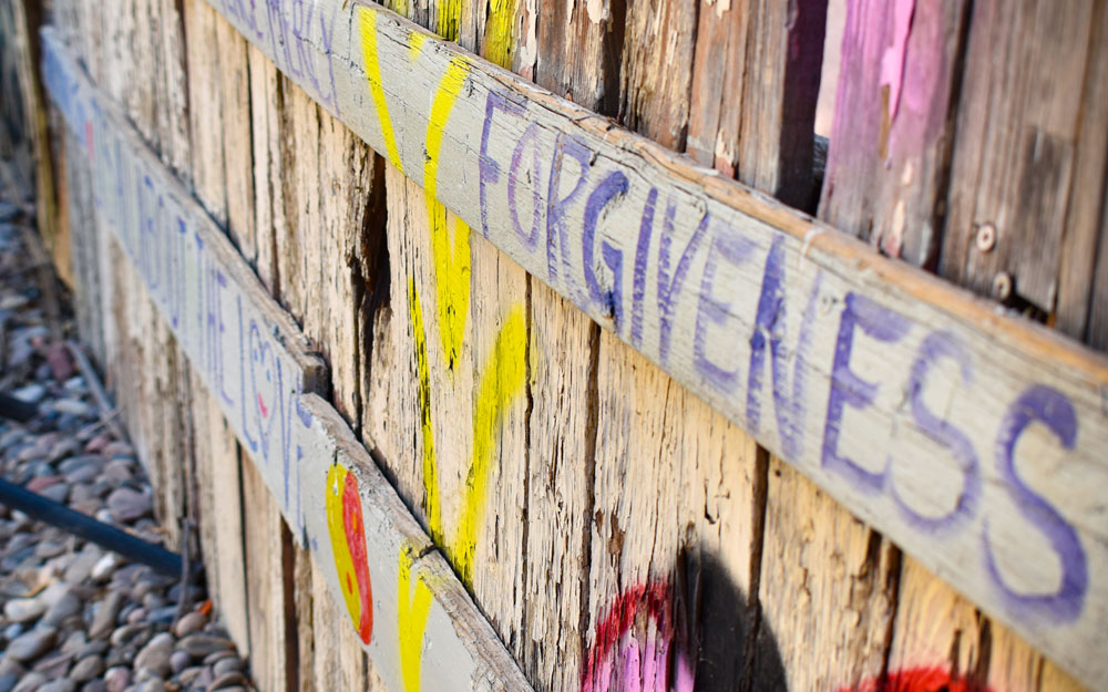 A multicolored fence mural reads “forgiveness”. This fence was painted by former HopeWorks clients.