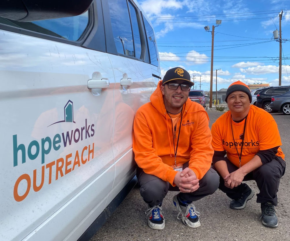 Two smiling outreach staff standing next to a HopeWorks van.
